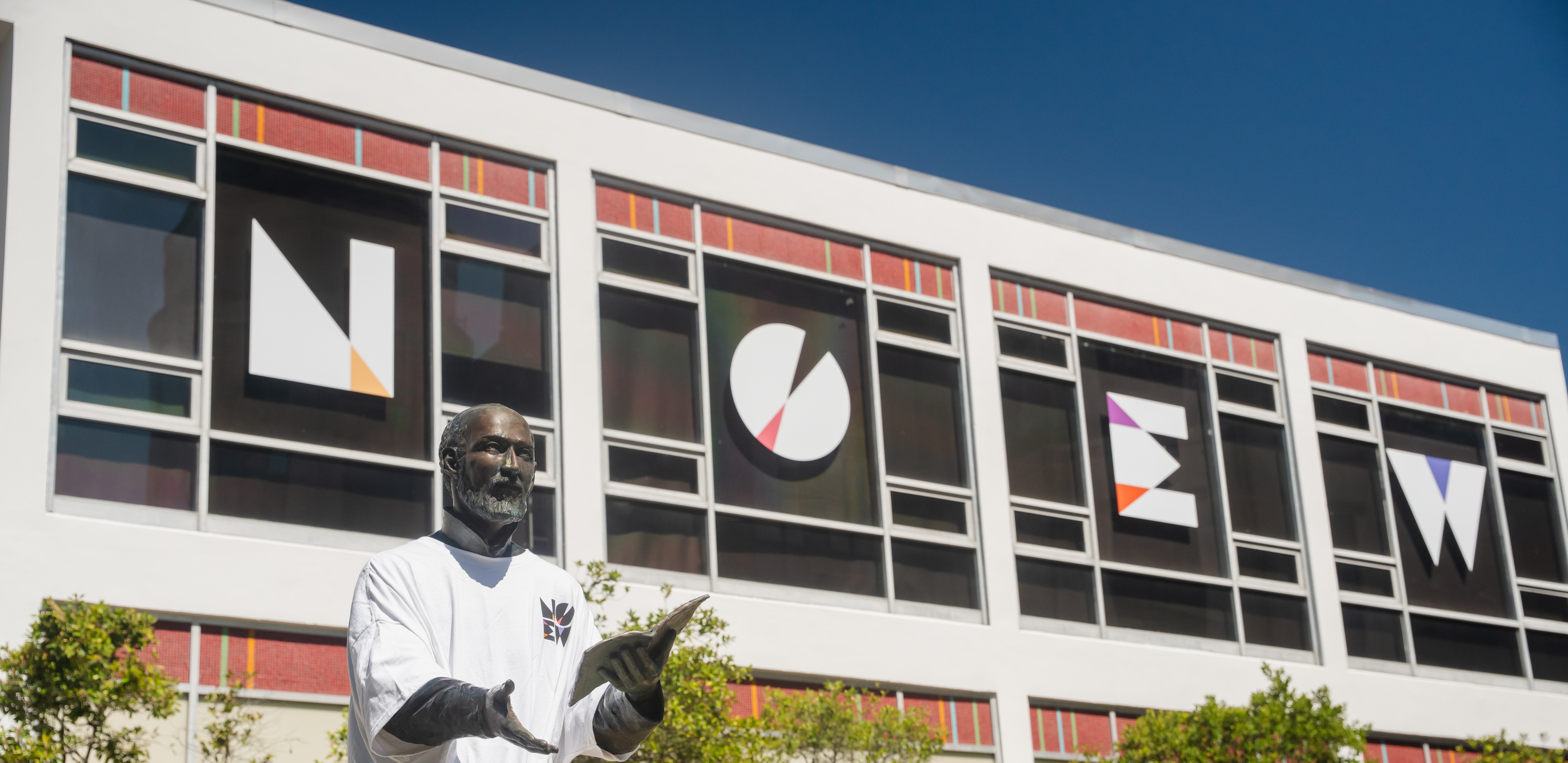 Letters NOEW on the Danna Center with the statue of St. Ignatius in the forefront wearing a NOEW white t-shirt